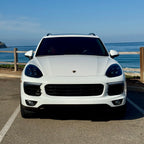 White Porsche Cayenne parked by a coastal road with ocean view